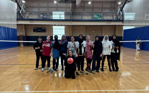A smiling girls volleyball team posing in front of the net.