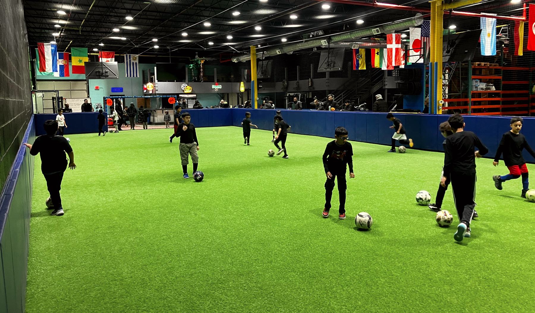 Boys dribbling soccer balls across an indoor turf field.